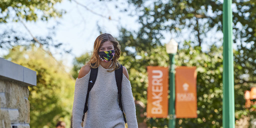 Female student walking on campus with a mask on.